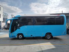 a large blue bus parked in a parking lot next to a white building with windows