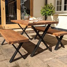 a wooden table with two benches next to it on a brick patio area in front of a house