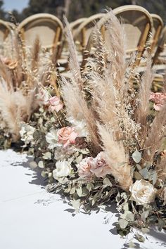 some chairs are lined up with flowers and feathers on them for an outdoor wedding ceremony