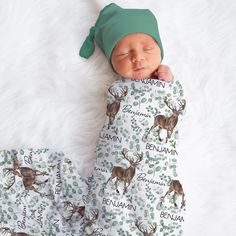 a baby sleeping on top of a white blanket next to a green beanie hat