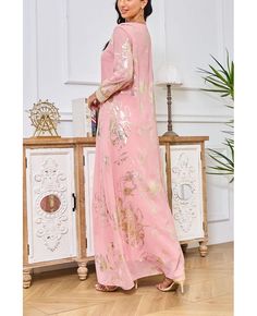 a woman standing in front of a table wearing a pink dress with gold embroidery on it