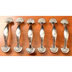 six silver spoons are lined up on a wooden counter top, each with an ornate design