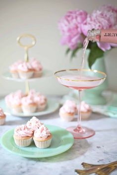 pink cupcakes are sitting on green plates with gold rimmed glasses and flowers in the background