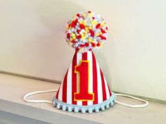 A mini size red/white stripe fabric party hat with red/yellow #1, baby blue pom pom trim on bottom and a matching yarn pom pom on top.  Attached to a 1/8" elastic to wear comfortable like a headband. 3"x4.25"  *Photos 2-3 just to show size on a 1-year old.  *Can be made with any number- just leave note in comments section- if nothing if noted #1 will be shipped.  DOGS:  If you are purchasing for a dog, please provide head measurement- start at top got down under chin and back to where started. * Customize colors- just leave a note in the comment section or message me. I make matching high chair banners and cake toppers too! Fun Hats For Birthday And Carnival, Playful Hats For Birthday And Carnival, Fun Carnival Birthday Hats, Fun Birthday Carnival Hats, Playful Mini Hats For Birthday And Carnival, Playful Mini Hats For Birthday Carnival, Playful Mini Hats For Carnival Birthday, Playful Red Hats For Playtime, Playful Red Hat For Playtime