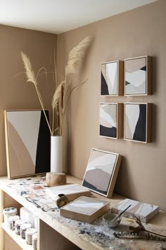 a table with some art on it in front of a vase and two framed pictures