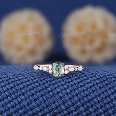 an oval cut green and white diamond ring on top of a blue cloth with three balls in the background