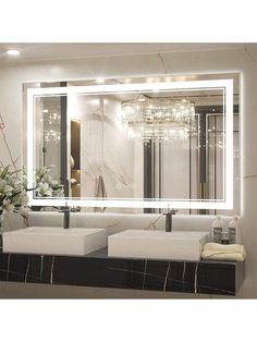 a bathroom vanity with two sinks and a large mirror above it that has lights on