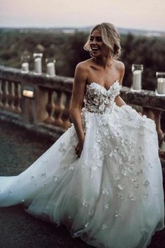 a woman in a white wedding dress standing on a balcony looking at the camera and laughing