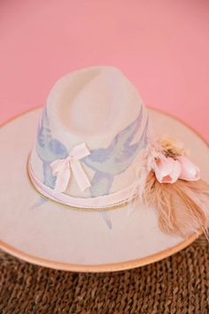 Add a touch of whimsy to your wardrobe with our SONGBIRD RANCHER HAT. This cream hat features charming gold accents and a playful design of blue birds. The beige feather and pink flower combo adds the perfect touch. Stand out from the crowd with this unique and stylish accessory. Cream Hat, Bird Birthday, Rancher Hat, Blue Birds, Birthday Hat, Song Bird, Spring 2024, Playful Design, Pink Flower