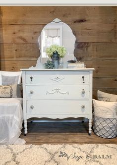 a white dresser sitting next to a bed with pillows on top of it and a mirror above it