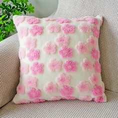 a pink and white pillow sitting on top of a couch next to a potted plant