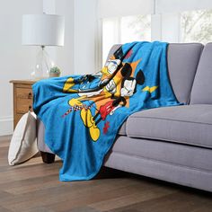 a couch with a blanket on it that has mickey mouse on it and is sitting in front of a window