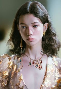 a close up of a person wearing gold jewelry and a pink dress with sequins on it