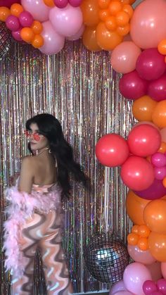 a woman standing in front of balloons and streamers with her face painted pink, orange and white