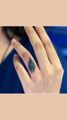 a woman's hand with a peacock feather tattoo on the middle finger and ring