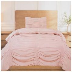 a bed with pink comforter and pillows on it in front of a wooden headboard