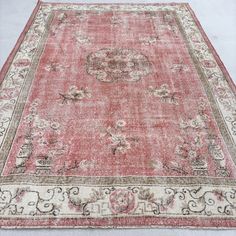 an antique rug with red and beige colors on the ground, in front of a white wall