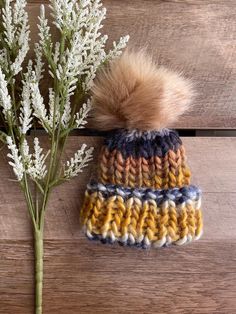 a crocheted hat with a pom - pom sits next to a flower