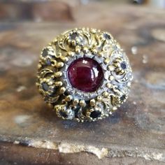 This Victorian Ruby Ring Made Of 2 Tones . Top Yellow 18k Yellow Gold Alloy With A Semiprecious Cabochon Ruby And Faceted 8 Smokey Topaz Set All Around The The Top. The Body Or Band Is Made Of Sterling Silver , Weights 16.7 Grams , Made By Hand With The Best Material And Love ! Bwood ,Metal Box Included !!! Luxury Ruby Ring With Multi-stone Round Cut, Luxury Multi-stone Ruby Ring, Luxury Multi-stone Round Cut Ruby Ring, Luxury Round Cut Multi-stone Ruby Ring, Round Gold Gemstones Fine Jewelry, Exquisite Multi-stone Yellow Gold Ruby Ring, Heirloom Gemstone Dome Ring For Formal Occasions, Multi-stone Diamond Jewelry With Round Stones, Elegant Multi-stone Dome Ring For Anniversary