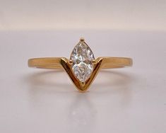 a yellow gold ring with a pear shaped diamond in the center, on a white surface