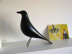 a black bird sitting on top of a white shelf next to a painting and a pair of glasses