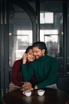 a man and woman sitting at a table with coffee cups in front of their faces