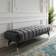 a gray bench sitting on top of a wooden floor next to a rug and potted plant