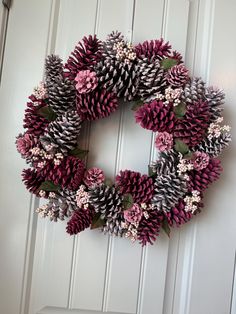 a wreath made out of pine cones is hanging on the front door with pink flowers