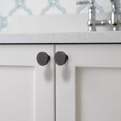 a kitchen sink with two black knobs on the front and back of the cabinet