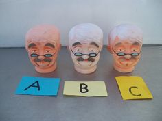 three plastic heads with glasses and mustaches are next to letters that spell out the word abc