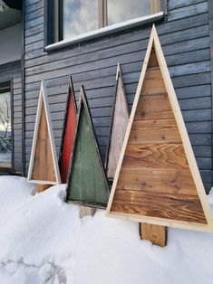 three wooden christmas trees in front of a house with snow on the ground and windows