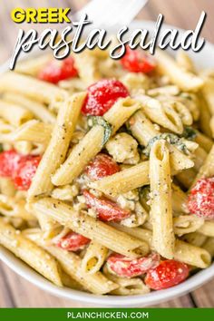 a white bowl filled with pasta covered in pesto and strawberries next to a fork