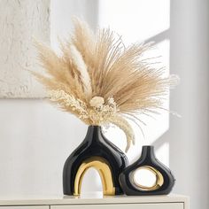 two black and gold vases sitting on top of a white dresser next to a window