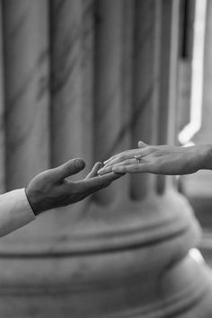 two people reaching out their hands to each other in front of a building with columns