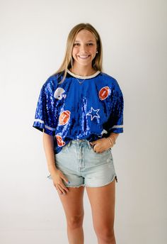 Get ready for game day with X's and O's Royal Blue Sequin Top! This top is not only fun, but also the perfect addition to your wardrobe. Pair it with your favorite shorts for a winning look! Fits true to size, Morgan is wearing a medium. She is 5'7, a size 6 and a 34C Varsity Tops For Cheerleading During Football Season, Collegiate Blue Tops For Cheerleading, Varsity Style Tops For Football Season Game Day, Cheerleading Fan Apparel Tops For Football Season, Blue Top For College Football Season, Sporty Crew Neck Top For Tailgating, Blue Tops For Football Season Fan Gear, Blue Short Sleeve Top For Cheerleading, Blue Tops For Cheerleading With School Spirit Style