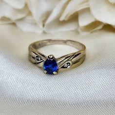 "Dainty 10k white gold ring featuring a prong set pear-shaped lab Sapphire and a small diamond chip on either side of the center stone. Stamped \"10k\" on the inside of the band. There is another hallmark however, there is some wear and is not legible. Size 5¾ US. Some patina to the band. In otherwise lovely vintage condition." Classic Teardrop Diamond Ring With Accent Stones, Pear-shaped Birthstone Promise Ring, Silver Teardrop Ring With Diamond Accents, Classic Teardrop Sapphire Ring For Anniversary, Formal Pear-shaped Birthstone Ring, Teardrop Diamond Accent Promise Ring, Fine Jewelry Pear-shaped Birthstone Promise Ring, Teardrop Diamond Accented Promise Ring, Teardrop Promise Ring With Diamond Accents