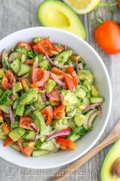 a white bowl filled with cucumber, tomatoes and onions next to sliced avocado