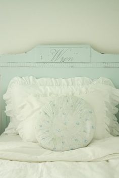 a white bed topped with pillows next to a wooden headboard