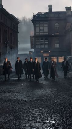 a group of men walking down a street next to tall buildings on a foggy day