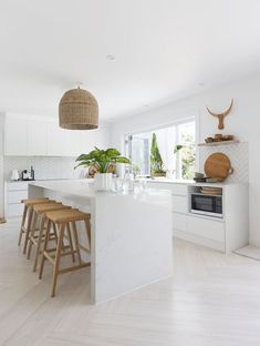 a white kitchen with wooden stools next to an island in front of a window