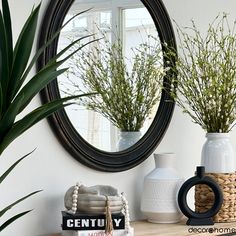 a mirror sitting on top of a wooden table next to a vase filled with plants