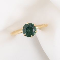 a close up of a ring with a green stone in it on a white cloth