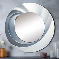 a round mirror sitting on top of a table next to vases and flowers in front of a gray wall