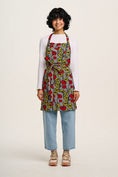 a woman standing in front of a white wall wearing an apron and smiling at the camera