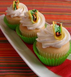 three cupcakes with white frosting and toppings on a green plate next to a red napkin