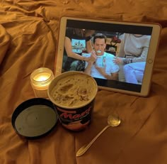 an ipad and some food are on a bed with orange sheets, candles and spoons