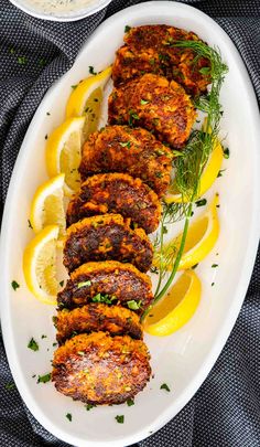 a white plate topped with crab cakes next to lemon wedges and garnished with herbs