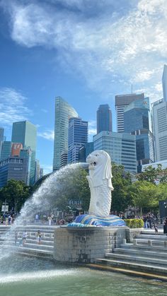 the water spouting from the statue is spraying up in front of the cityscape