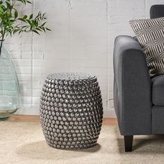 a living room with a gray couch and white brick wall in the background, along with a vase filled with green plants