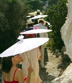 a woman in a red dress holding an umbrella over her head while standing next to other people